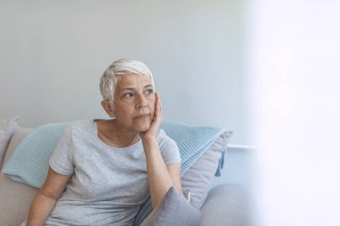 Olgun gri saçlı kadın evde poz kanepede oturan.