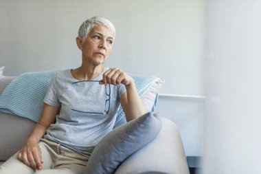 Olgun gri saçlı kadın evde poz kanepede oturan.