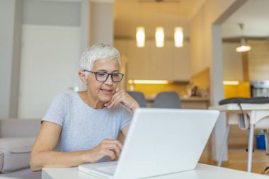 Evde dizüstü bilgisayar üzerinde çalışan olgun kadın.