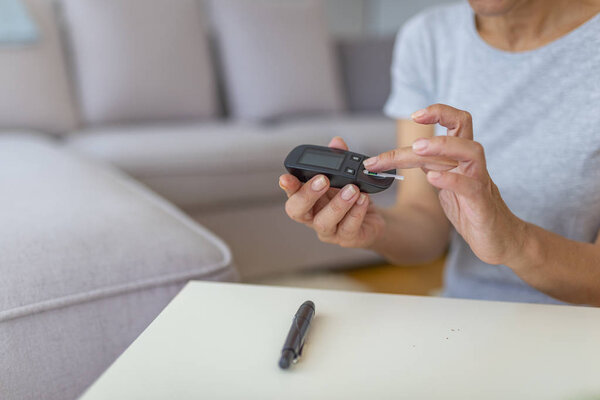 Close-up photo of woman testing level of glucose in blood. Mature woman using lancet and glucometer doing blood glucose measurement.