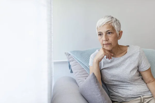 Mature grey haired woman sitting on sofa posing at home.