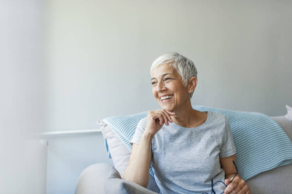 Happy woman relaxing on her couch at home in the sitting room. Portrait of beautiful mature woman smiling while sitting at sofa at home. Beautiful middle age woman smiling at home