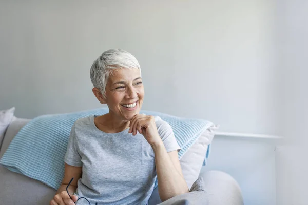 Portrait of beautiful mature woman smiling while sitting at sofa at home. Happy woman relaxing on her couch at home in the sitting room. Shot of a mature woman relaxing at home