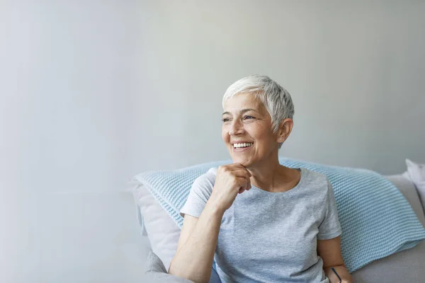 Portrait of beautiful mature woman smiling while sitting at sofa at home. Happy woman relaxing on her couch at home in the sitting room. Shot of a mature woman relaxing at home