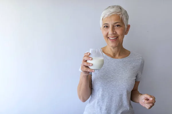 Portrait of mature woman with glass of milk. Woman in grey T-shirt with glass of milk.