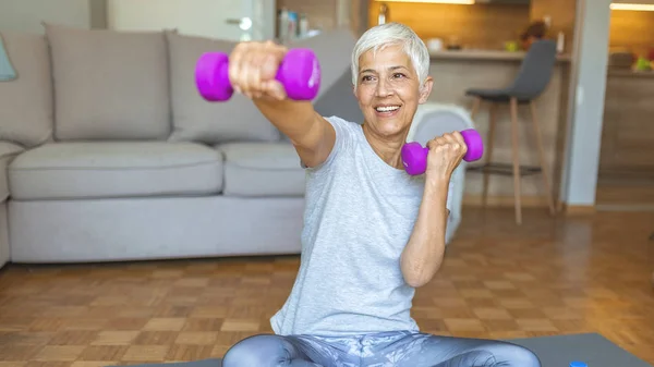 Staying fit is one way to age with grace. Nice elderly woman taking pleasure in the workout. Active senior woman at home exercising with weights. Mature Woman Exercise At Home.