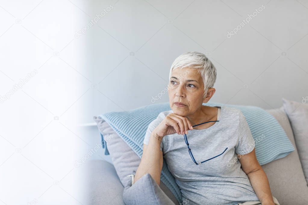 Mature grey haired woman sitting on sofa posing at home.