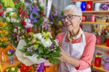 Bir çiçekçi dükkanında çalışan ve güneşli bir gün boyunca yeni bir çiçek düzenleme yapma çekici bir çiçekçi iş kadını sahibinin Gülümseyen portresi. Küçük işletme sahibi.