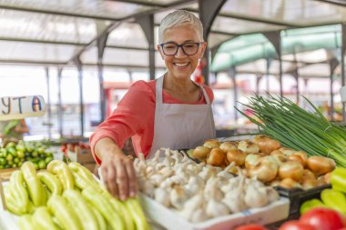 Dost bir kadın bir çiftçinin marketinde organik sebze tezgahı ve bahçeden taze sebze satan eğilimi. Çiftçiler Taze Gıda Pazarı'nda Kadın Tezgah Sahibi
