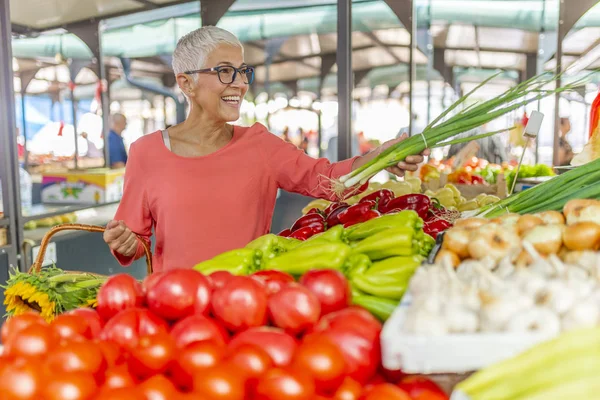 Mature Female Customer Shopping At Farmers Market Stall. Woman shopping at local Farmers market. Mature woman buying vegetables.