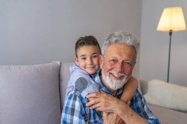 Gülümseyen büyükbaba ve torun kanepede oturuyor. Büyükbaba ve torunu gri arka planda gülümsüyor. Aile, nesil, ilişkiler ve insan kavramı - Mutlu dedesi ve torunu