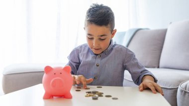 Kumbarada para biriktiren bir çocuk. Küçük Çocuk kumbaradan para topluyor. Küçük çocuk bozuk paralarla oynuyor yığınlar yapıyor. Finansal sorumluluğu öğrenme ve tasarruf kavramını planlama