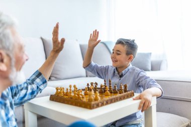 Büyükbaba ve torun satranç oynuyor. Büyükbaba ve torun. Genç çocuk evde dedesi ile satranç oynuyor. Büyükbaba ve torunu evde masada birlikte satranç oynuyorlar.