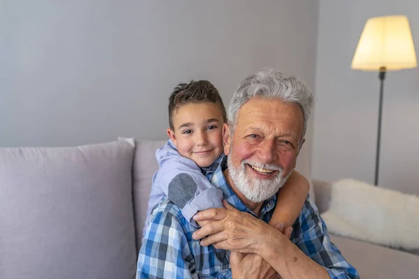 Smiling grandfather and grandson sitting on sofa. Grandfather and grandson smiling on grey background. Family, generation, relations and people concept - Happy grandfather and grandson