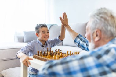 Mutlu büyükbaba küçük torunu ile satranç oynar. Mantık ve stratejik düşüncenin gelişimi. Genç çocuk evde dedesi ile satranç oynuyor. Mutlu çocuk torunu yaşlı yaşlı adam ile satranç oynarken 