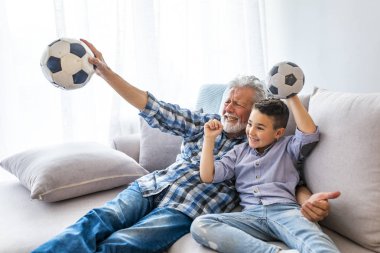 Dedesi ile kanepede küçük çocuk, bir futbol oyunu için tezahürat ve bir futbol topu tutan. Dedesi ile kanepede küçük çocuk, bir futbol oyunu için tezahürat ve evde bir futbol topu tutarak... 