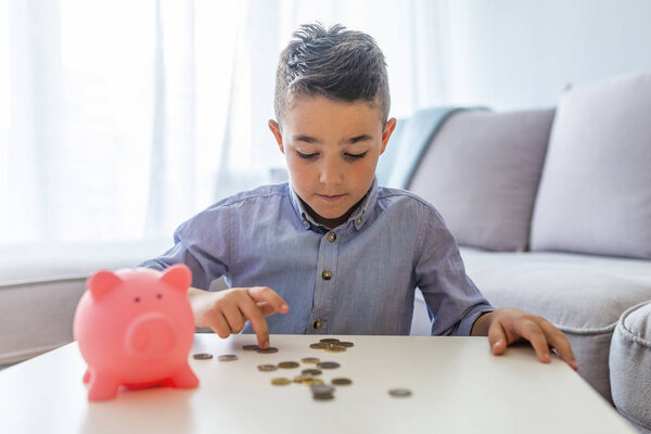 Закрыть Маленький мальчик экономит деньги в копилке свиньи сосредоточиться на мальчике. Детство, деньги, инвестиции и счастливые люди концепция - улыбающийся маленький мальчик с копилкой свиньи и деньги дома
 