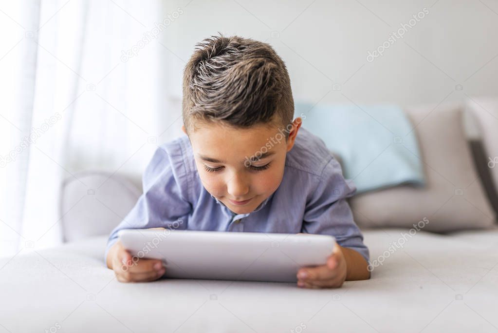 Boy playing with digital tablet. Little boy lying on the sofa and using digital tablet. Little boy with digital tablet sitting on sofa, on home interior background