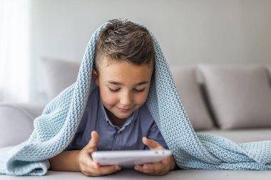 Dijital tablette çizgi film izleyen küçük çocuğun yakın çekim. Çocuk e-kitabı okur. Küçük çocuk tabletin ekranına bakar ve gülümser. Küçük çocuk evde dijital tablet ile oynarken gülümsüyor