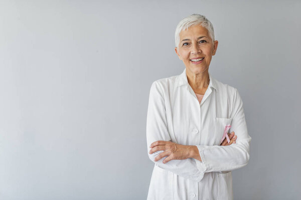 Keeping you healthy is my priority. Confident serious mature woman doctor. Portrait of senior female doctor looking at camera. Woman hospital worker looking at camera and smiling, studio, grey background