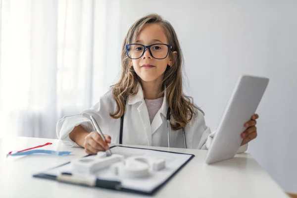 Little doctor. Cute little girl with stethoscope and tablet playing at home. A little cute smiling girl wearing a doctor uniform with stethoscope. Little girl playing a doctor on white background