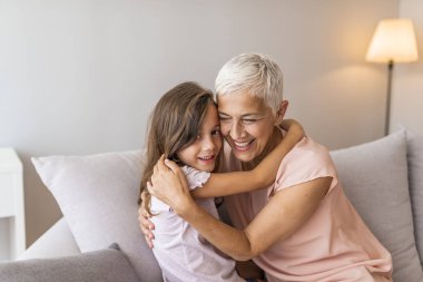 Eğleniyor sevimli küçük kız kanepede birlikte yalan kucaklayan gülümseyen Büyükanne ile oynarken, mutlu büyükanne ve okul öncesi torun dinlenmek kanepeye, Büyükanne Torunu evde gülüyor sarılma