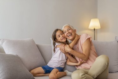 Büyükanne ve torun kucaklama. Küçük sevimli kız ve büyükannesi evde birlikte vakit geçiriyorlar. Kanepede otururken eğlenmek, sarılmak ve gülümsemek.