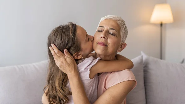 Granddaughter embracing her grandmother in living room. Her granddaughter holds the key to her heart. Grandmother and granddaughter. Smiling senior woman and girl embracing