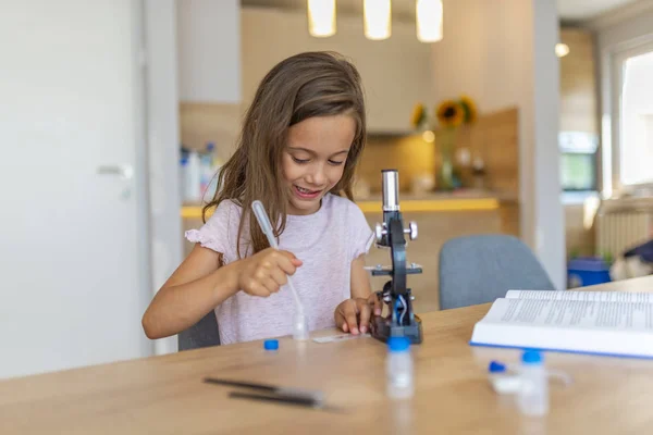 Little girl concentrates while using microscope. Studying chemistry. Confident little girl uses microscope at home. Schoolgirl using microscope.