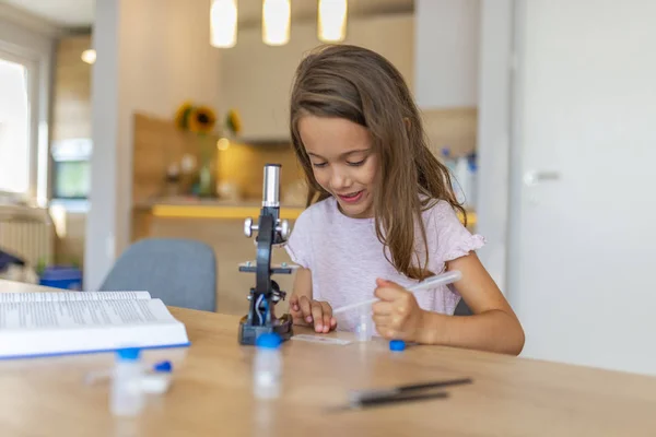 Preschool age girl looks into microscope. Child playing science in the kitchen at home. Cute little girl looking through the microscope. Little girl uses microscope