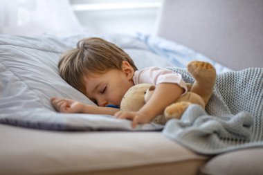 Sevimli kızıl saçlı bebek kanepede peluş oyuncak ile uyku. Sabah uykusu. Oyuncak ayıyla uyuyan bebek. Küçük tatlı yürümeye başlayan çocuk yatağında uyuyor