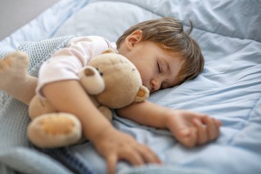 Uykucu. Genç çocuk mavi bir yastıkta huzur içinde uyuyor. Bebeğin uykuya ihtiyacı var! Bebek çocuk oyuncak ayı ve emzik ile uyuyor. Yumuşak battaniye ile kaplı bebek uyku 