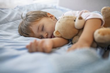 Sevimli kızıl saçlı bebek kanepede peluş oyuncak ile uyku. Sabah uykusu. Oyuncak ayıyla uyuyan bebek. Küçük tatlı yürümeye başlayan çocuk yatağında uyuyor
