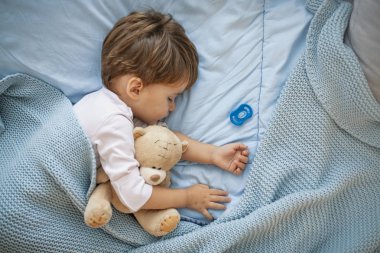Evde yatakta uyuyan sevimli küçük çocuk. Yatakta uyuyan bir bebek, elinde oyuncak ayı. Tatlı rüyalar. Evde kanepede yatarken uyuyan küçük bir bebek. Oyuncak ayıyla yatakta uyuyan çocuk
