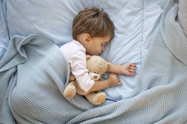 Oyuncak ayı ile birlikte uyuyan erkek bebek fotoğrafı. En sevdiği uyuklama yeri. Oyuncakla yatakta uyuduktan sonra sevimli çocuk çocuk. Oyuncak ayıyla yatakta uyuyan çocuk. Uykucu