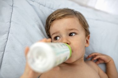 Kanepede yatan şişeden süt tutan ve besleyen erkek bebek portresi. Mavi battaniyenin üzerinde süt şişesi olan sevimli bir erkek bebek. Uyuma zamanı. 