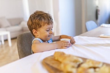Süt ya da yoğurt içen sevimli çocuk. Süt bıyıklı sevimli erkek bebek, kapalı portre. Sağlıklı yiyin. Toddler atıştırmalık yiyor. Sağlıklı beslenme. Süt iç. Çocuk sevimli bebek kahvaltı yeme. 