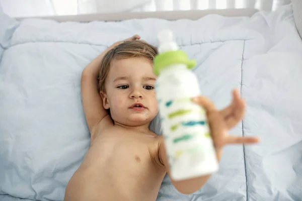 ミルクを愛する男の子 ソファの上に横たわっているボトルからミルクを飲む赤ちゃん ボトルを持った赤ちゃん 甘い面白い赤ちゃんの飲み物 ミルクボトル付き赤ちゃん — ストック写真