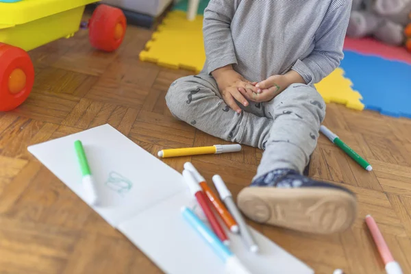 Boy drawing with felt-tip pen lying down on the wooden floor in the living room at home. Family activity concept. Small boy child drawing with colorful marker pen.