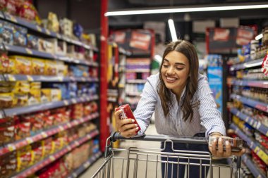 Süpermarket koridorunda alışveriş arabası olan bir kadın. Marketten yiyecek almak. Market alışverişi. Marketten alışveriş yapan genç ve güzel bir kadın. 