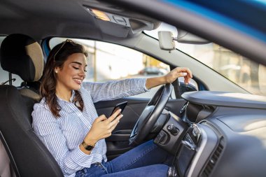 Araba sürerken akıllı telefonuyla mesaj atan genç bir kadının portresi. İş kadını arabada oturuyor ve akıllı telefonunu kullanıyor. Kadın sürücü ve telefon ekranlı maket resmi