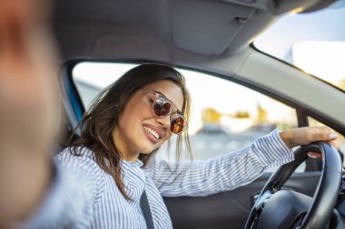 Yolculuk selfie 'si. Akıllı telefonunu kullanan ve araba kullanırken selfie çeken genç bir kadın. Arabada akıllı telefon kamerasıyla selfie çeken genç bir kadın. Gülümseyen genç kadın selfie çekiyor.