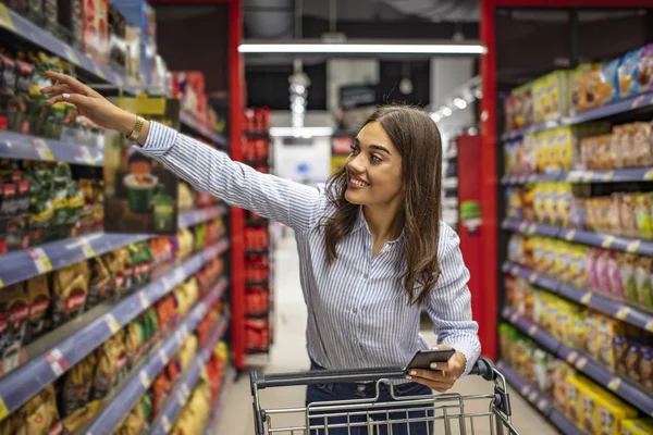 Foto Jovem Mulher Alegre Supermercado Com Carrinho Compras Escolhendo Produtos — Fotografia de Stock