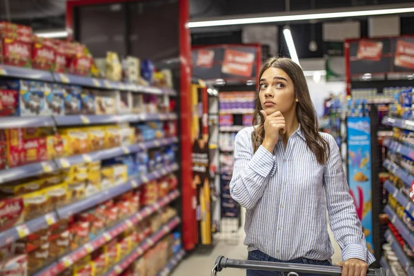 Jovem Mulher Olhando Confuso Escolher Produtos Corredor Supermercado Andando Com — Fotografia de Stock