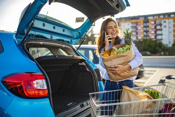 Woman multi-tasking getting in the car after shopping at the grocery store. Bringing in the Shopping. Happy girl packing groceries. Woman putting bags into car after shopping