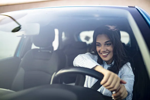 美しい若い幸せな笑顔の女性は日没時に彼女の新しい車を運転する 若い女性が市内で車を運転している 車の中で美しい女性の肖像画 窓の外を見て笑顔 — ストック写真
