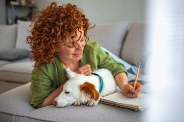 Bir kız deftere yazar ve bir köpekle oynar. Kızıl saçlı kadın gülümsüyor, evde köpeğe sarılıyor. Evde bir melezi barındırmak. Yaşam tarzı. Üniversiteliler Okuma Öğrenme Dersleri Notları