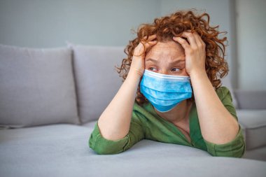Tıbbi maskeli genç bir kadın kendini karantinaya almak için evde karantinada kalıyor. Ev karantinası, COVID-19 önleme, Coronavirüs salgını durumu. Evde koruyucu maskeli bir kadın var..