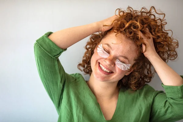 Laughing girl applying beauty mask on her face. Skin care. Cute redhaired girl with natural skin. Beauty cosmetic concept. Isolated on grey background. Beautiful smiling woman with face mask