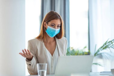 Ofiste dizüstü bilgisayarla çalışan koruyucu maskeli bir iş kadını. Milenyum kadın çalışan koruyucu yüz maskesi ve tıbbi eldivenlerle çalışan koruyucu şirket çalışanı iş yerinde dizüstü bilgisayarda çalışarak virüsü 19 tehlikeli karantina altında tutuyor.